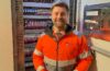 Stephen in a high-vis jacket stood next to a cupboard filled with electrical switches.