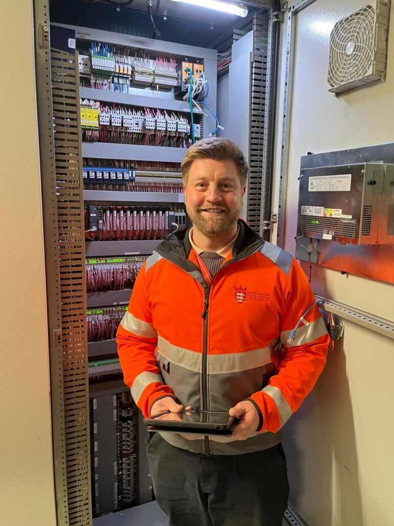 Stephen in a high-vis jacket stood next to a cupboard filled with electrical switches.